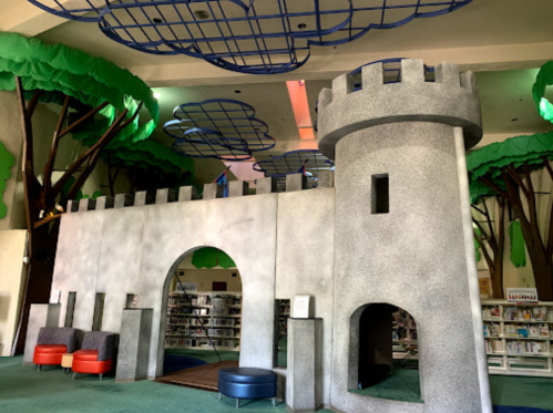 A whimsical library interior featuring a castle structure and large tree-like decorations on the ceiling.